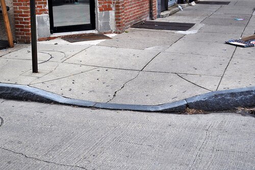 A sidewalk with a dip that allows objects with wheels easy access to the sidewalk.